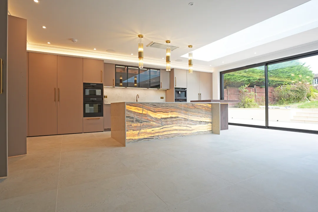 A Madisons kitchen project with an illuminated stone island, pendant lights and wide garden doors.